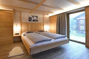 A modern bedroom with a wooden bed, a large window, and a view of a building outside. - Holiday apartment in Au with swimming pool (Au)