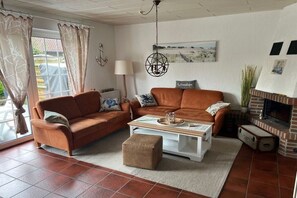 A living room with two sofas, a coffee table, a fireplace, and a window with curtains. - Holiday home with 3 bedrooms (Wangerland)