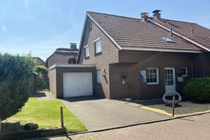 A two-story brick house with a garage, a paved driveway, and a well-maintained lawn. - Holiday home with 3 bedrooms (Wangerland)