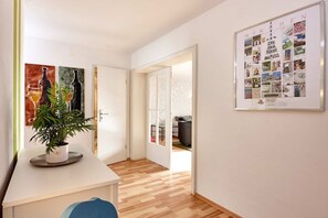 A hallway with a white door leading to a room, a framed collage on the wall, and a potted plant on a white table. - Holiday apartment with 2 bedrooms (Garmisch Partenkirchen)