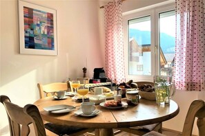 A dining table with breakfast items, chairs, a window with curtains, and a painting on the wall. - Holiday apartment with 2 bedrooms (Garmisch Partenkirchen)