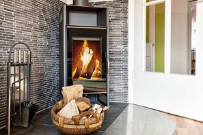A modern fireplace with a visible fire, a metal radiator, and a basket of firewood on a tiled floor. - Holiday apartment with 2 bedrooms (Garmisch Partenkirchen)