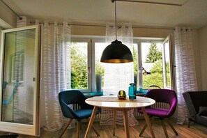 A room with a round table, two chairs, a hanging light fixture, and a view through large windows. - Alpine Flair Holiday Apartment 101 Zeitgeist (Oberstdorf)