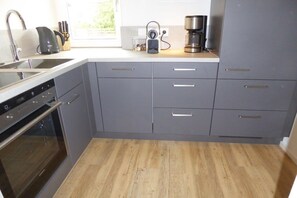 A kitchen with grey cabinets, a stainless steel sink, and a coffee maker. - Alpine Flair Holiday Apartment 101 Zeitgeist (Oberstdorf)