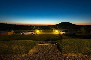 A nighttime outdoor area with two cars parked facing each other, a pathway leading to a building, and a hill in the background. - Holiday home with 3 bedrooms (Jelenia Gora)