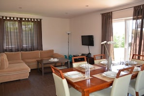 A furnished living room with a sofa, dining table set for four, and a flat-screen TV mounted on the wall. - Holiday home with 3 bedrooms (Jelenia Gora)