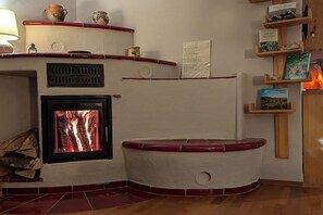 A fireplace with a fire, a shelf with books, and a wall-mounted clock. - Holiday apartment with 1 bedroom (Badenweiler OR Sehringen)
