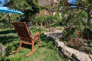 A wooden rocking chair in a garden with a stone wall and various plants. - Holiday apartment with 1 bedroom (Badenweiler OR Sehringen)