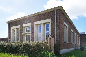 A two-story brick building with a flat roof, multiple windows, and a small garden area with a wooden gate. - Duinweg 4a - Apartment A (Huisduinen)