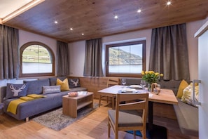 Un espacio de sala acogedor con sofá, mesa de centro y mesa de comedor, ventanas amplias con cortinas, y vistas al exterior.