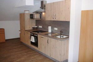 A compact kitchen with wooden cabinets, a microwave, a sink, and a stove. - At the bricklayer's - Alpine rose (Hopferau)