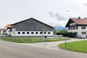 A building with a large wooden structure, a fenced area, and a road in front. - At the bricklayer's - Alpine rose (Hopferau)