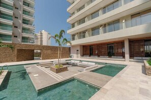 A modern outdoor pool area with a geometric design, surrounded by a building with balconies and a stone wall. - Nácar Blue Suite | Beach, Luxury, and Comfort (Santa Marta)