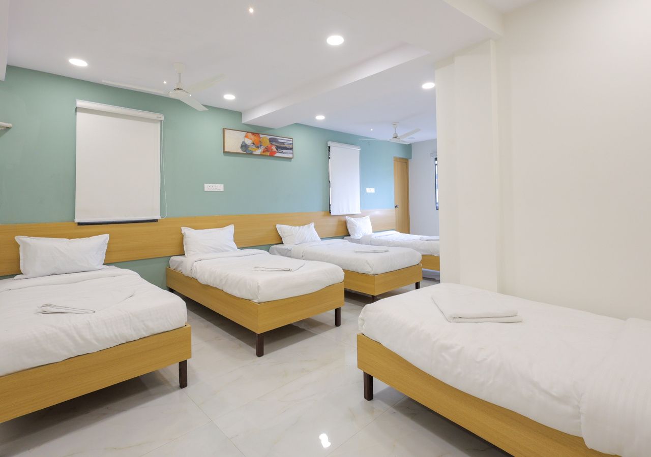 Habitación de hotel con cuatro camas individuales, ventilador de techo, luces empotradas y un ventanal grande.