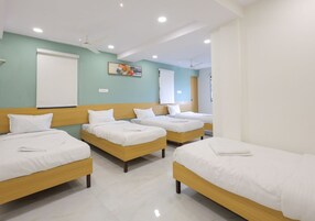 Habitación de hotel con cuatro camas individuales, ventilador de techo, luces empotradas y un ventanal grande.