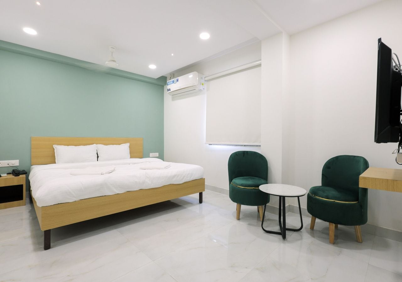 Ein modernes Hotelzimmer mit einem Bett, zwei Stühlen, einem kleinen Tisch und einer Klimaanlage.