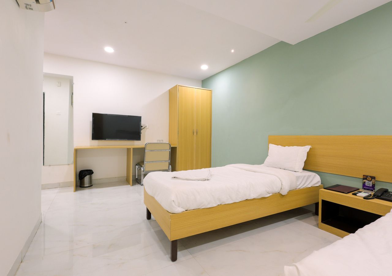 A hotel room with a bed, bedside table, a desk with a chair, a television, and a wardrobe.