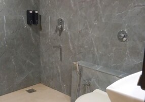 Un baño con pared de mármol, ducha y retrete.
