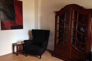 A room with a black armchair, a wooden cabinet with glass doors, and a small table with a hat on it. - Holiday home in Ahr Valley with 1 bedroom (Ahrweiler)