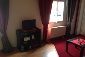 Ein Zimmer mit einer schwarzen Unterhaltungsecke, einem roten Teppich, einem Fenster mit Vorhängen und einer Heizung.