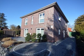 A two-story brick house with a paved driveway and a small garden area. - Holiday apartment with 1 bedroom (Norden)