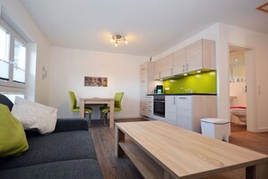 A modern kitchen with white cabinets and a green countertop, a dining area with a table and chairs, and a grey sofa with green cushions. - Holiday apartment with 1 bedroom (Norden)