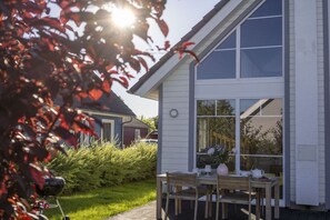 Ein Haus mit Terrasse, Grill und Tisch mit Stühlen.