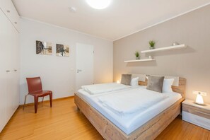 A modern bedroom with a wooden bed frame, a single chair, and wall-mounted shelves with plants. - Delbrück-Villen D125 Vacation Rental on the Beachfront in Heringsdorf (Heringsdorf (Seebad))