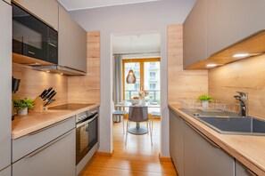A modern kitchen with wooden cabinets, a built-in oven, and a dining area with a table and chairs. - Delbrück-Villen D112 Vacation Rental on the Beachfront in Heringsdorf (Heringsdorf (Seebad))