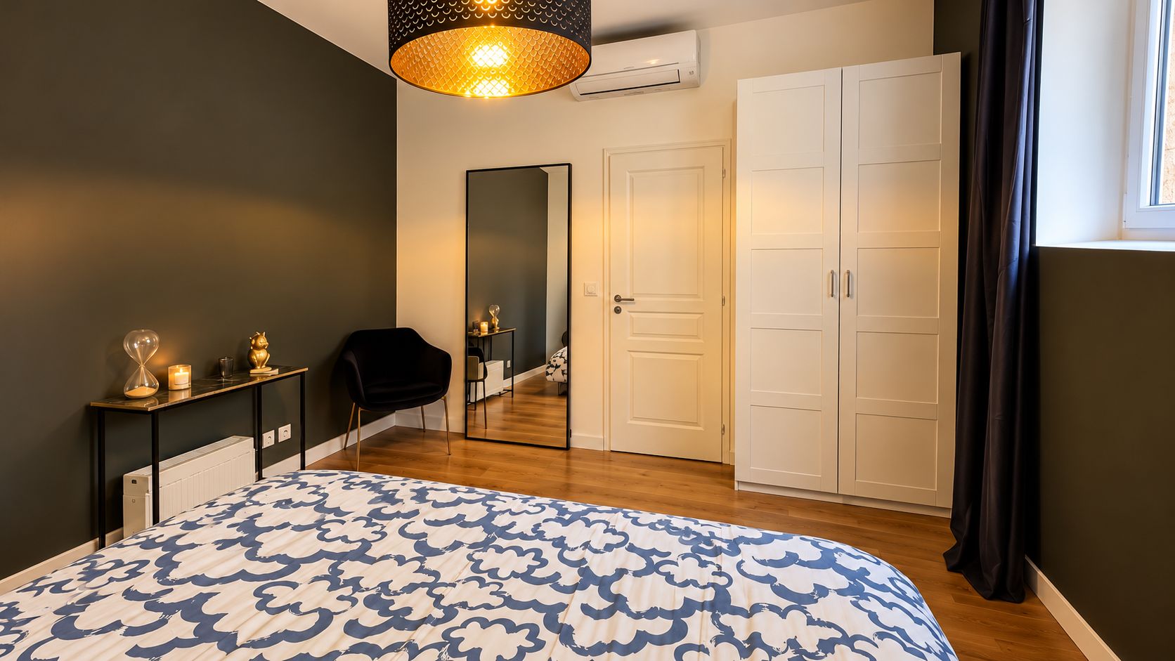 A bedroom with a bed, a bedside table, a mirror, a wardrobe, and a door leading to a bathroom.