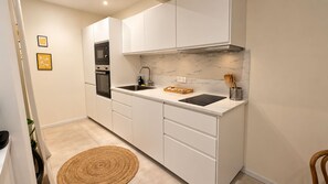 Une cuisine compacte avec des meubles blancs, un four encastré, un évier et un plan de travail en marbre.
