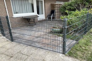 Un patio clos avec une table et des chaises, une plante en pot et un mur en briques.