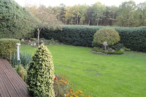 A well-maintained garden with a wooden deck, neatly trimmed hedges, and a variety of plants. - Holiday home in Neuenkirchen with barbecue (Neuenkirchen)