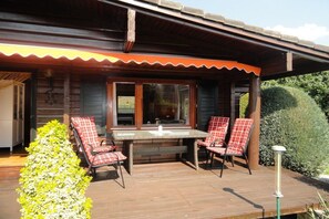 A wooden deck with a table and four chairs, surrounded by greenery. - Holiday home in Neuenkirchen with barbecue (Neuenkirchen)