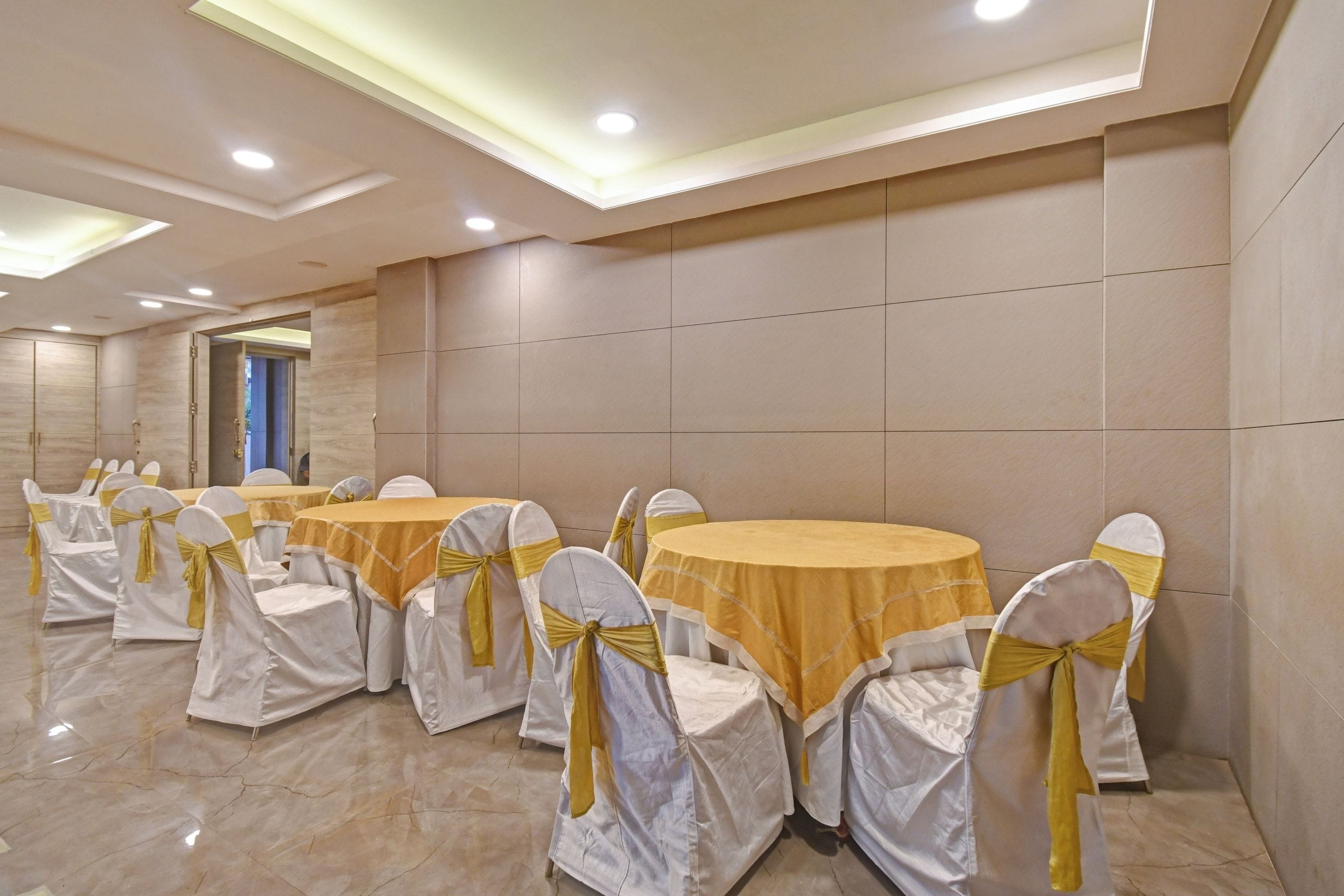 A conference room with round tables and chairs, each with a white cover and a yellow ribbon.