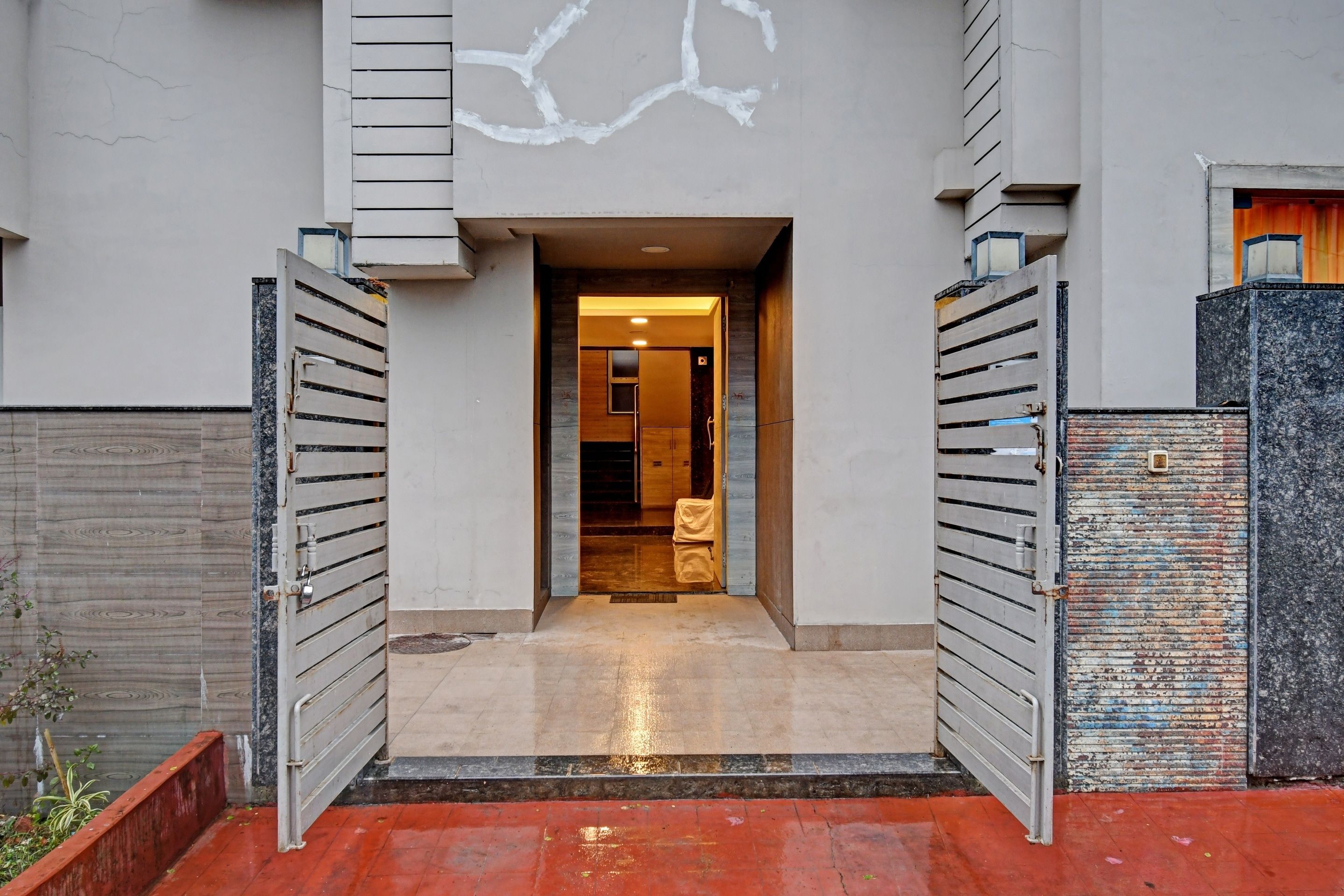 Une entrée moderne avec un portail en métal, un chemin en béton et une porte en bois donnant accès à un bâtiment.
