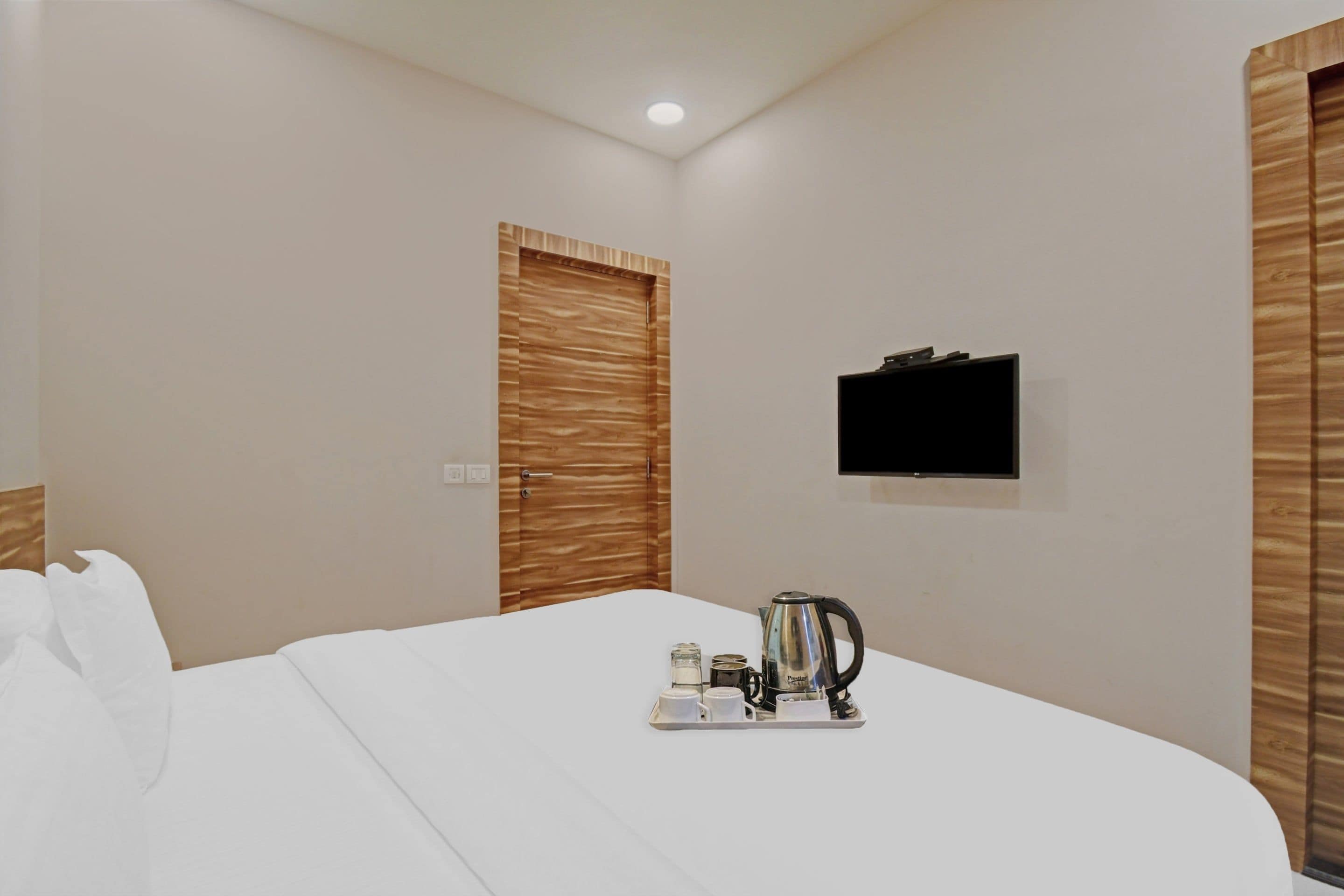 A hotel room with a bed, a television mounted on the wall, and a tray with a kettle and cups.