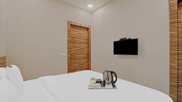A hotel room with a bed, a television mounted on the wall, and a tray with a kettle and cups.
