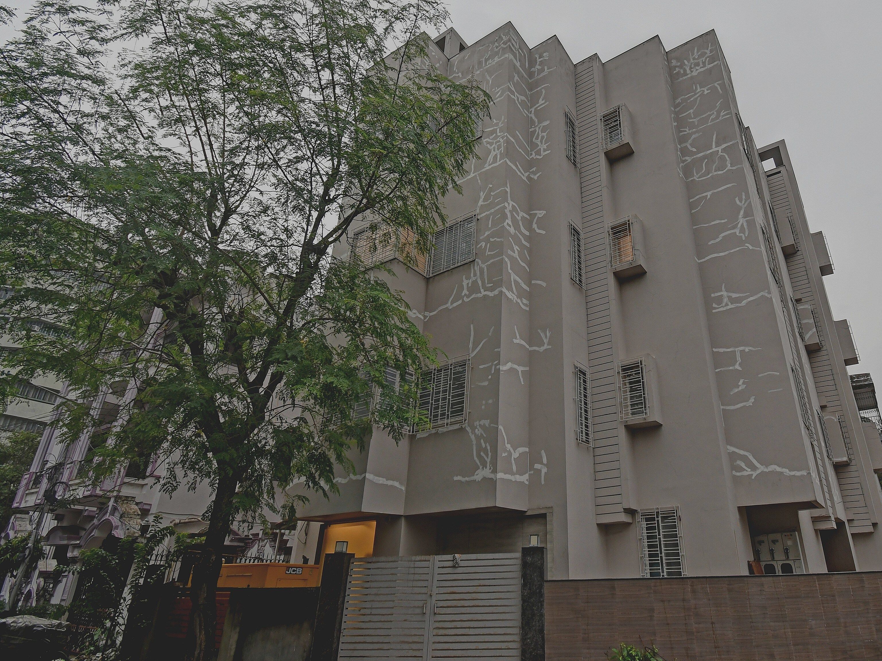 Un edificio de varios pisos con un diseño arquitectónico moderno, que incluye balcones y una entrada protegida por un portón.