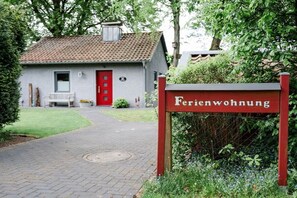 A building labeled 'Ferienwohnung' with a red door, a bench, and a pathway leading to it. - Holiday home with 1 bedroom (Hermannsburg)