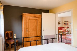 A bedroom with a bed, a wooden wardrobe, a chair, and a door leading to another room. - Holiday home with 1 bedroom (Hermannsburg)