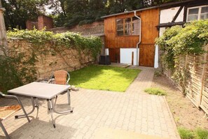 Ein kleiner Garten mit gepflasterter Terrasse, einem Tisch mit Stühlen und einem Holzschuppen.