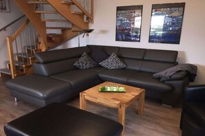 A modern living room with a sectional sofa, a wooden coffee table, and a staircase. - Holiday home with 2 bedrooms (Greetsiel)