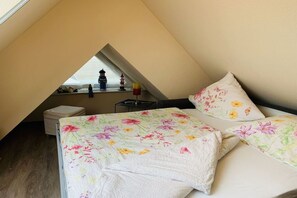 Een slaapkamer met een schuine kap, een bed met bloemenbedrukking, een nachtkastje en een raam met uitzicht op een vuurtoren.