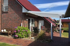 A brick house with a red roof, a covered patio area, and outdoor furniture. - Holiday home with 2 bedrooms (Greetsiel)