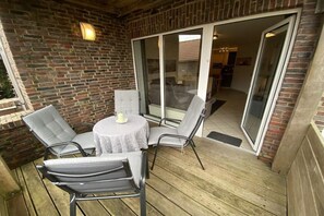 An outdoor patio with a round table and four chairs, a brick wall, and a sliding glass door leading to an interior space. - Holiday apartment ""Nei Ut"" (Borkum)