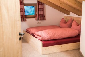 A bedroom with a wooden bed frame, red bedding, and a window with curtains. - Holiday apartment in Fischen-Berg with Wi-Fi (Fischen- Berg)