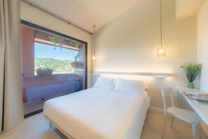 A bedroom with a bed, a desk, and a window with a view of greenery. - Elgiò (Taormina)