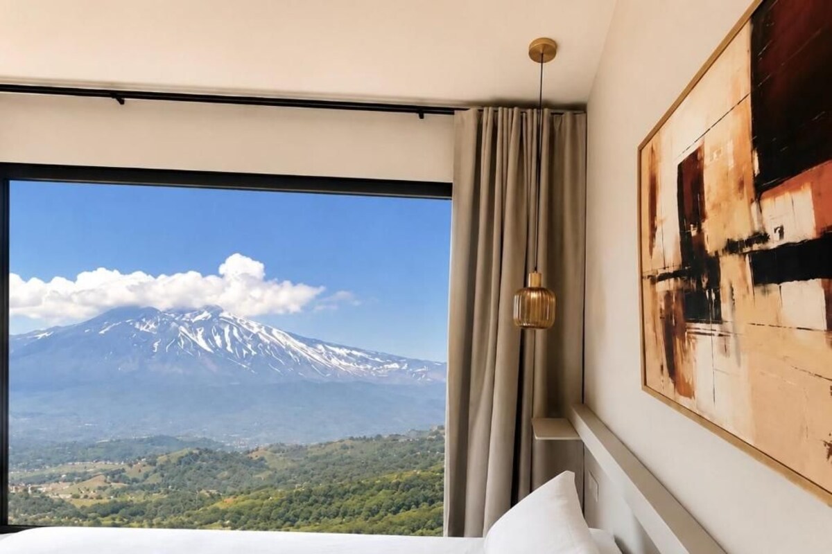 Una habitación de hotel con una cama, un ventanal grande y un cuadro en la pared.