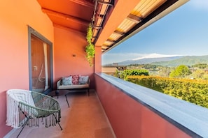 A balcony with a cushioned seating area, a wicker chair, and a view of a mountainous landscape. - Elgiò (Taormina)